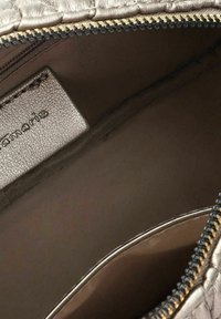 Interno grigio metallico di una borsa con zip, caratterizzato da una finitura testurizzata, con una fodera liscia e un'etichetta del marchio visibile.
