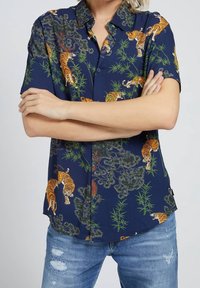 Tmavě modrá košile s krátkým rukávem zdobená tygrem a bambusovým vzorem, vyrobená z lehké látky, s límečkem na knoflíky a volným střihem.