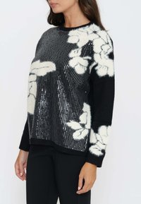 Maglione nero con motivi floreali bianchi, texture paillettata su un lato e finitura morbida e pelosa. Polsini e colletto a costine.