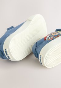 Chaussures en tissu bleu avec semelles en caoutchouc blanc, présentant un motif de personnages de dessin animé sur le côté et une texture antidérapante sous la semelle.