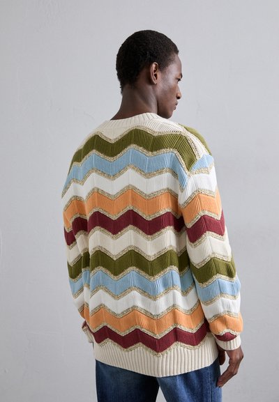 Adīta džemperis ar zigzaga rakstu krēmkrāsā, zaļā, zilā, sarkanā, oranžā un zelta krāsā. Tam ir brīva piegriezuma forma un ribas aproces.