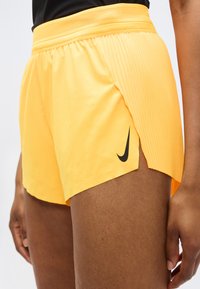 Σορτς τρεξίματος Nike σε ζωντανό κίτρινο χρώμα, με αεριζόμενη ζώνη μέσης από διχτυωτό ύφασμα, πλαϊνές σχισμές και μαύρο λογότυπο.