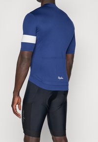 Maillot de cyclisme bleu à manches courtes, bande d'accent blanche et poches arrière. Associé à un short de cyclisme rembourré noir avec détail logo.