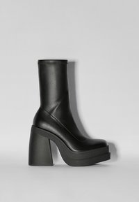 Botas negras de tobillo con un acabado de cuero suave, suela de plataforma gruesa y tacón cuadrado ancho. Presenta un eje ajustado y un detalle de costura minimalista.