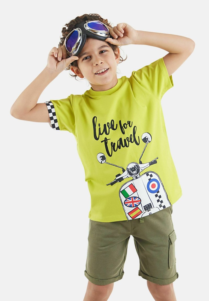 Camiseta de color verde lima con un diseño gráfico de un scooter que incluye banderas y el texto "vive para viajar." Con mangas cortas y detalles a cuadros.