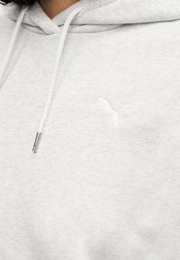 Ανοιχτό γκρι φούτερ με κουκούλα από μαλακό ύφασμα, με λευκό κεντημένο λογότυπο στο στήθος και κουκούλα με κορδόνια και μεταλλικές άκρες.