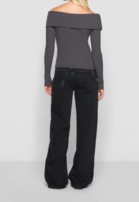 Grå off-the-shoulder topp med långa ärmar, som matchas med högmidjade, löst sittande svarta jeans med en lätt slitningseffekt.