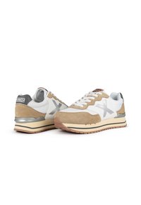 Las zapatillas presentan una combinación de cuero blanco y gamuza marrón, detalles en plata, una suela intermedia blanca gruesa y una suela exterior de goma texturizada.
