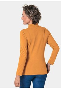Langärmliger Rollkragenpullover in Senfgelb, aus weichem Material gefertigt. Hat eine figurbetonte Silhouette und ein glattes, einfaches Design ohne Verzierungen.