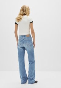 Vit kortärmad skjorta med svart kant, i kombination med ljusblå högmidjade utsvängda jeans med bakfickor och en märkespatch.