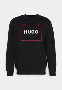 Sudadera negra de manga larga, con puños acanalados y un escote redondo. Presenta un contorno rectangular rojo con "HUGO" en blanco.