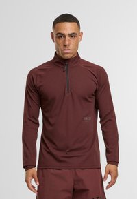 Bordeauxfarbendes, kurzärmeliges Sportshirt mit halbem Reißverschluss, aus strukturiertem Stoff, mit langen Ärmeln und kleinem Logo nahe dem Saum. Minimalistisches Design.