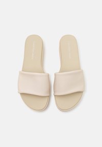 Beige slip-on sandals with a smooth fabric strap, contoured footbed, and minimalistic design. Subtle branding on the insole.