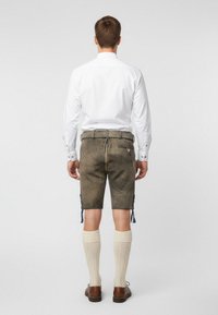 Lädershorts i en dämpad grön nyans med snörningar på sidorna, kombinerade med knälånga krämfärgade strumpor och bruna skor, sett bakifrån.
