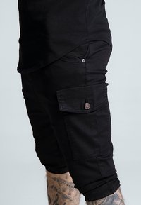 Zwarte cargoshorts met een slanke pasvorm, voorzien van een zijzak met knoopsluiting en opgerolde zomen. Gemaakt van duurzaam katoenmixmateriaal.