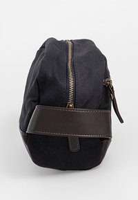 Kanvaspussukka merensinisenä, jossa on ruskea nahkapohja. Siinä on keskellä vetoketjusuljin, hoikka muoto ja sivukahva helppoa kantamista varten.