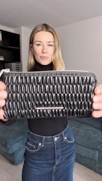 Black woven leather clutch with a textured surface, featuring a silver zipper and a rectangular metallic accent on the front.