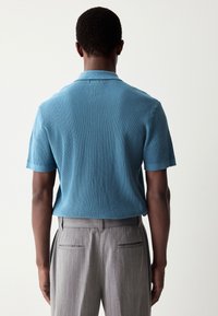 Kortärmad, ribbad blå stickad pikétröja kombinerad med ljusgrå randiga byxor, med en mjuk textur och klassisk krage.