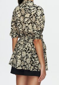 Blusa nera floreale con maniche a sbuffo, vita arricciata e orlo svasato. Presenta motivi floreali color crema e oro su un tessuto morbido.