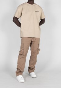 Beige bavlněné tričko s malým černým logem, spárované s světle hnědými kargo kalhotami s bočními kapsami a bílými teniskami.