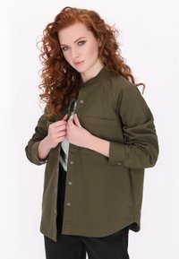 Camicia verde oliva con bottoni, colletto alto, tasca singola sul petto, maniche lunghe e vestibilità comoda. Design stile giacca con una texture liscia.