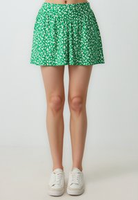 Gonna floreale verde con motivi bianchi, design a pieghe, vita elastica e forma svasata, abbinata a sneakers bianche.