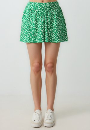 Jupe florale verte avec des motifs blancs, design plissé, taille élastique et forme évasée, associée à des baskets blanches.
