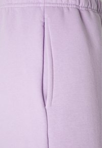 Lila mjukisbyxor i lätt lila färg, gjorda av mjukt material, med resårmidja och sidofickor, samt en slät yta.