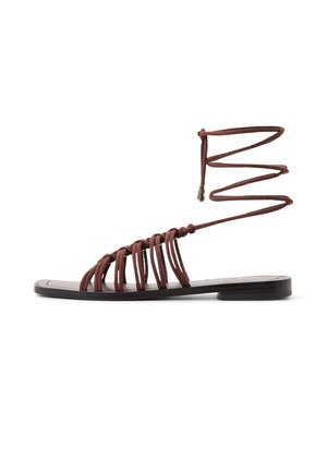 Bruine platte sandaal met meerdere dunne bandjes over de voet en lange veterstrikjes rond de enkel met metalen uiteinden.