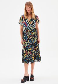 Robe portefeuille florale avec de courtes manches volantées, présentant des rayures colorées sur le corps et un fond sombre avec des fleurs éclatantes. Sandales à plateforme noires.