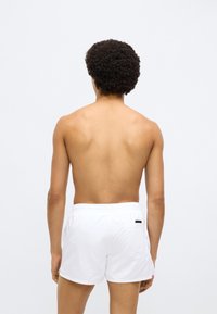 Valged ujumispüksid elastse vöökohaga ja tagataskuga. Kangas tundub kerge ja sile. Stiil on põlvekõrgune.