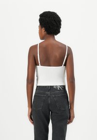 Cropped top bianco a righe con spalline sottili, abbinato a jeans in denim grigio scuro a vita alta. Presenta un cinturino con logo e tasche posteriori.
