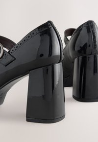 Scarpe nere in pelle verniciata con tacco a blocco, punte arrotondate, perforazioni decorative e cinturino con fibbia argentata sulla parte superiore.