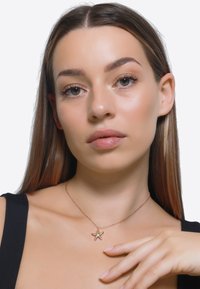 Gouden sterfispendant ketting op een delicate ketting, gedragen tegen een zwart shirt. Gladde textuur, minimalistisch ontwerp met een glanzende afwerking.