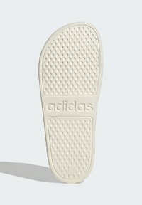 Adidas foam slide sole in off-white, featuring a textured grip pattern, rounded shape, and embossed logo for traction and comfort.