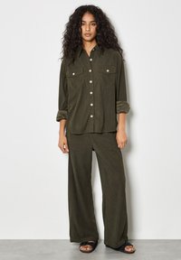 Koordiniertes Outfit in Olivgrün mit einem Hemd mit Knopfleiste und zwei Brusttaschen sowie weiten Hosen aus weichem, strukturiertem Stoff.