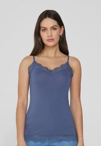 Granatowy top na ramiączkach z koronkowym wykończeniem przy dekolcie i brzegu, wykonany z gładkiego, elastycznego materiału. Cienkie, regulowane ramiączka.