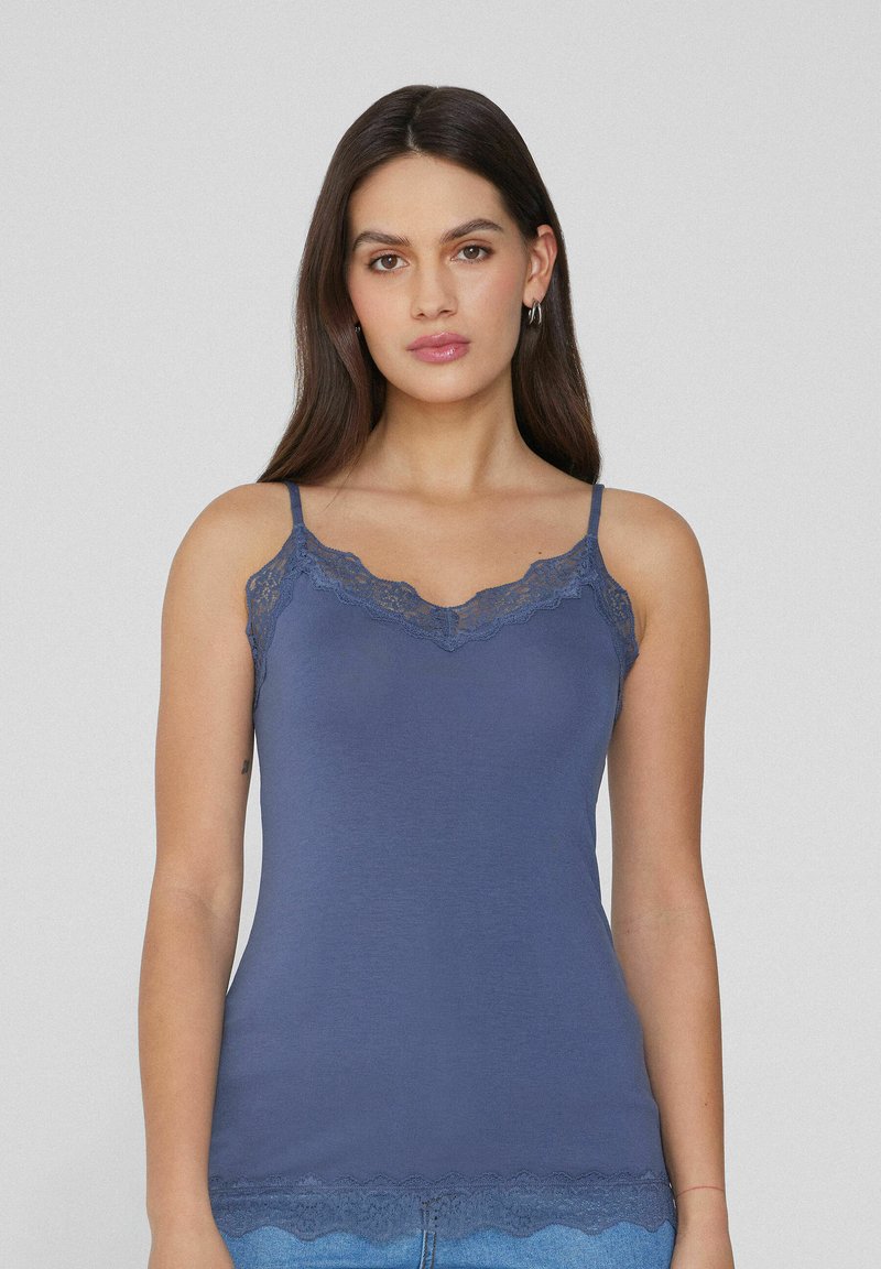 Granatowy top na ramiączkach z koronkowym wykończeniem przy dekolcie i brzegu, wykonany z gładkiego, elastycznego materiału. Cienkie, regulowane ramiączka.