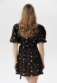 Vestido negro ajustado con patrones celestiales coloridos que incluyen estrellas, planetas y lunas; mangas cortas abullonadas; tejido suave y corbata ajustable.