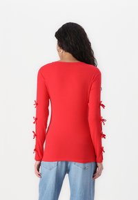 Rød langermet topp med rund hals og bånd på ermene. Myk stoff med en tettsittende design, kombinert med avslappede blå jeans.