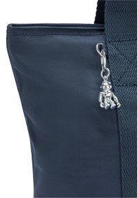 Sac en nylon bleu marine avec finition texturée, décoré d'un charm argenté, coutures renforcées et bandoulière noire robuste. Design simple avec des détails pratiques.