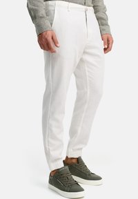 Pantalones jogger de lino blanco con puños elásticos y cierre de cremallera, combinados con zapatillas de deporte verde oscuro con suela blanca y logo.