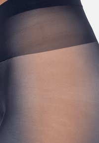 Transparente Strumpfhosen mit einem dunklen Bund, der in einen helleren Nude-Ton übergeht. Glatte Textur mit einem Farbverlauf zwischen den Farbtönen.
