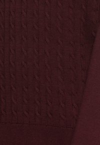 Burgundy stickad tyg med en texturerad kabelmönster och släta detaljer. Jämn sömnad och ribbade kanter ger definition.