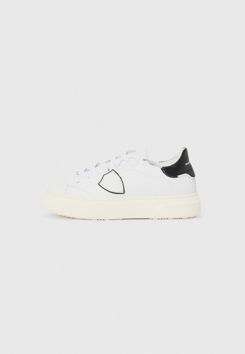 Białe skórzane sneakersy z teksturowanym czarnym obcasem. Posiadają okrągły czubek, wiązanie na sznurowadła oraz beżową gumową podeszwę z wzorem antypoślizgowym.