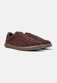 Brown suede sneakers with a smooth finish, round toe, and gray laces. Features a flexible tan rubber sole and a minimalist design.