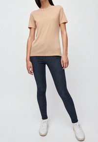 Camiseta de rayas beige claro con mangas cortas, combinada con jeans ajustados de mezclilla oscura y zapatillas blancas. Diseño simple con un corte relajado.