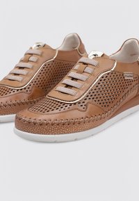Zapatillas de cuero marrón con diseño perforado, acentos trenzados, suela crema y cordones planos. Presenta un logo en el lateral y costuras decorativas.