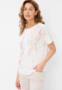 Hvid kortærmet t-shirt med blomstermønster i pink og grå. Blødt bomuldsstof med en afslappet pasform. Sømløs halsudskæring og sidesplitter.