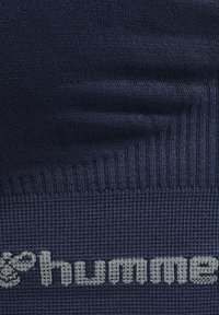 Gros plan sur un tissu tricoté bleu marine avec des motifs texturés et le mot partiellement visible « hume » en fil gris clair.